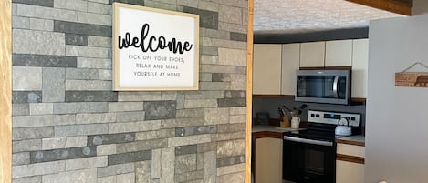 Une cuisine moderne avec un mur d’accent en pierre, un panneau d’accueil et un plafond en bois.