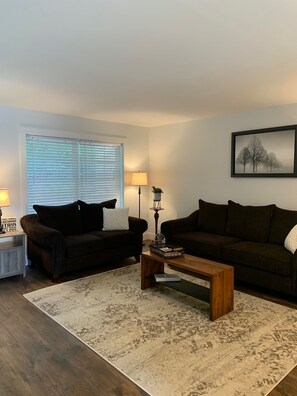 A living room with two dark sofas, a wooden coffee table, a patterned rug, a lamp, and a framed picture on the wall.