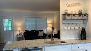 A modern kitchen with a granite countertop, stainless steel dishwasher, white cabinetry, and a coffee station with mugs and a coffee maker.