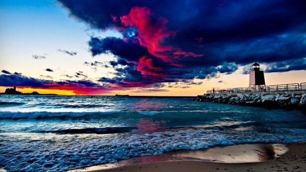 A coastal scene with a lighthouse, waves, and a sunset.