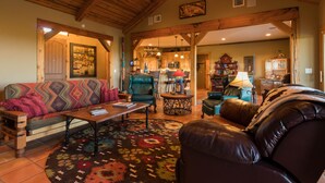 A spacious living room with a sofa, a leather armchair, and a coffee table. There is a kitchen in the background with a microwave and a refrigerator.