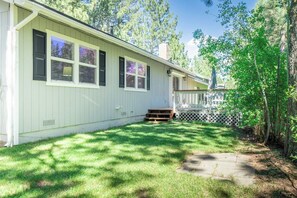 A single-story house with a covered porch, a fenced yard, and a tree.