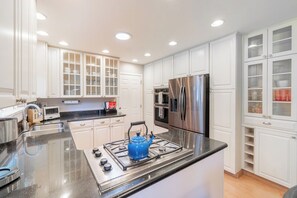 A modern kitchen with white cabinetry, stainless steel appliances, and a blue kettle on the stove.