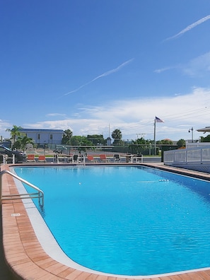 Una piscina con un cielo azul despejado, una bandera y un edificio al fondo.