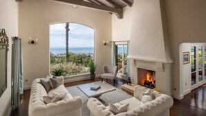 A living room with a fireplace, a sofa set, a coffee table, and a view of the ocean.