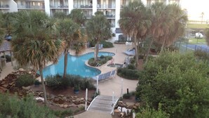 Un resort con piscina, palme e campo da tennis.