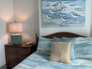 A bedroom with a bed, a nightstand, a lamp, and a painting of birds on the wall.