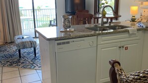 Una cucina con mobili bianchi, lavastoviglie integrata, lavello e zona pranzo con una sedia e un tavolo.