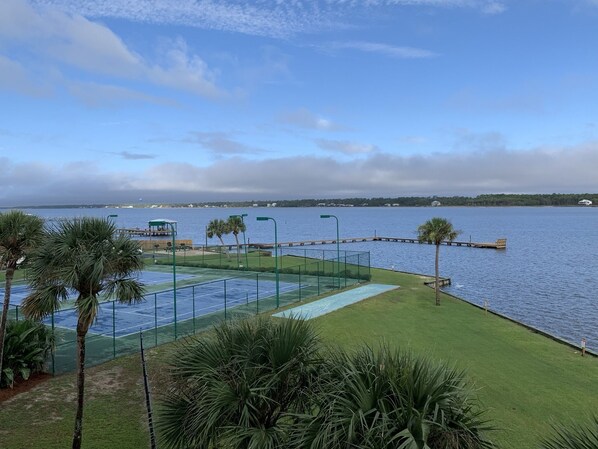 A tennis court with a view of the water and a dock.