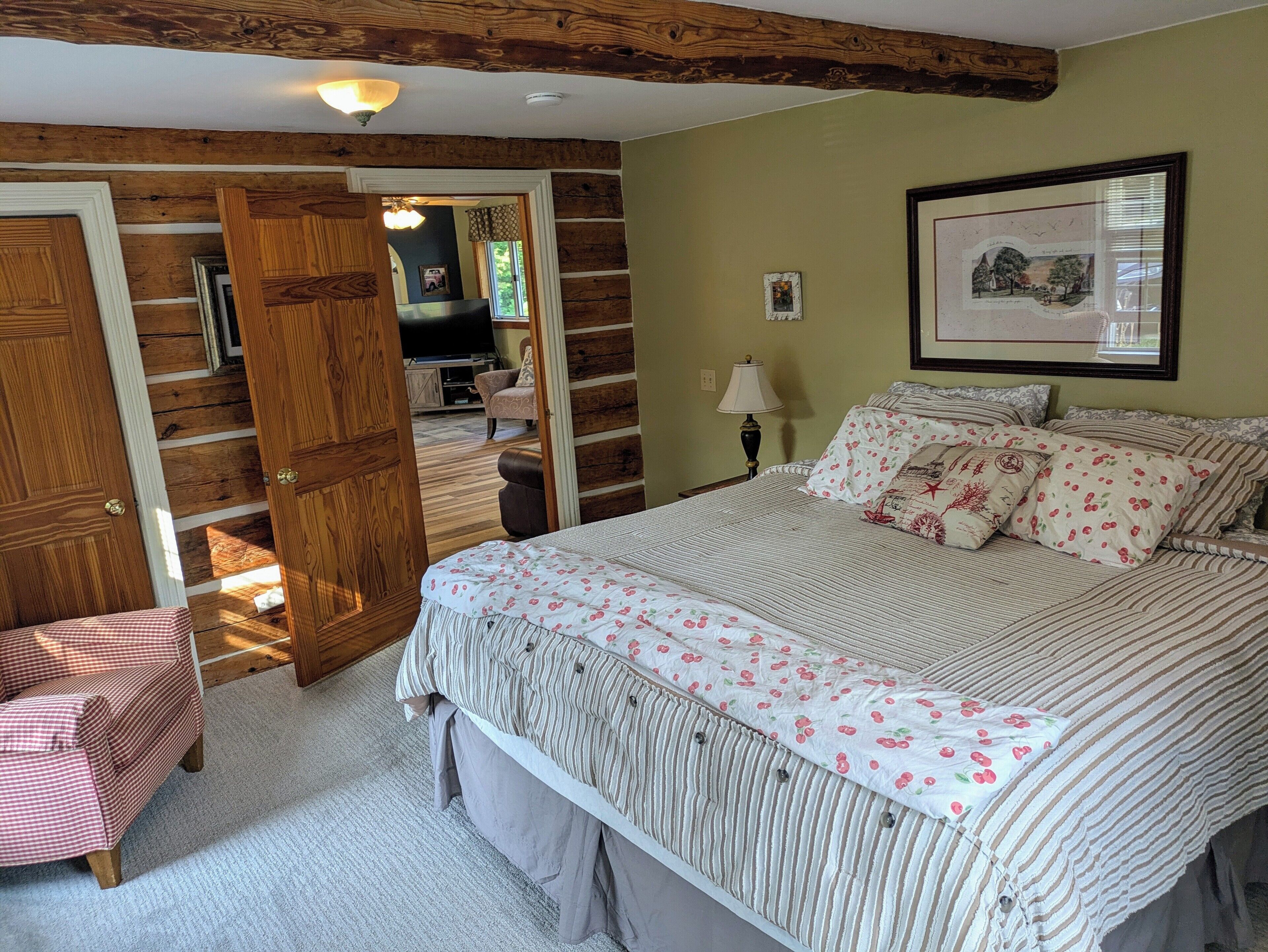 Quarto com cama, cadeira, porta de madeira, abajur e quadro na parede.