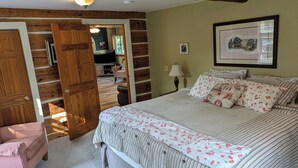 Un dormitorio con cama, una silla, una puerta de madera, una lámpara y un cuadro en la pared.