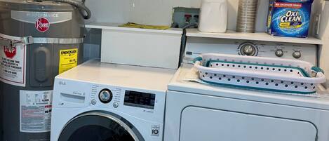 Un espace buanderie équipé d’un lave-linge et d’un sèche-linge à chargement frontal, d’un étendoir empilable et de divers produits de nettoyage.