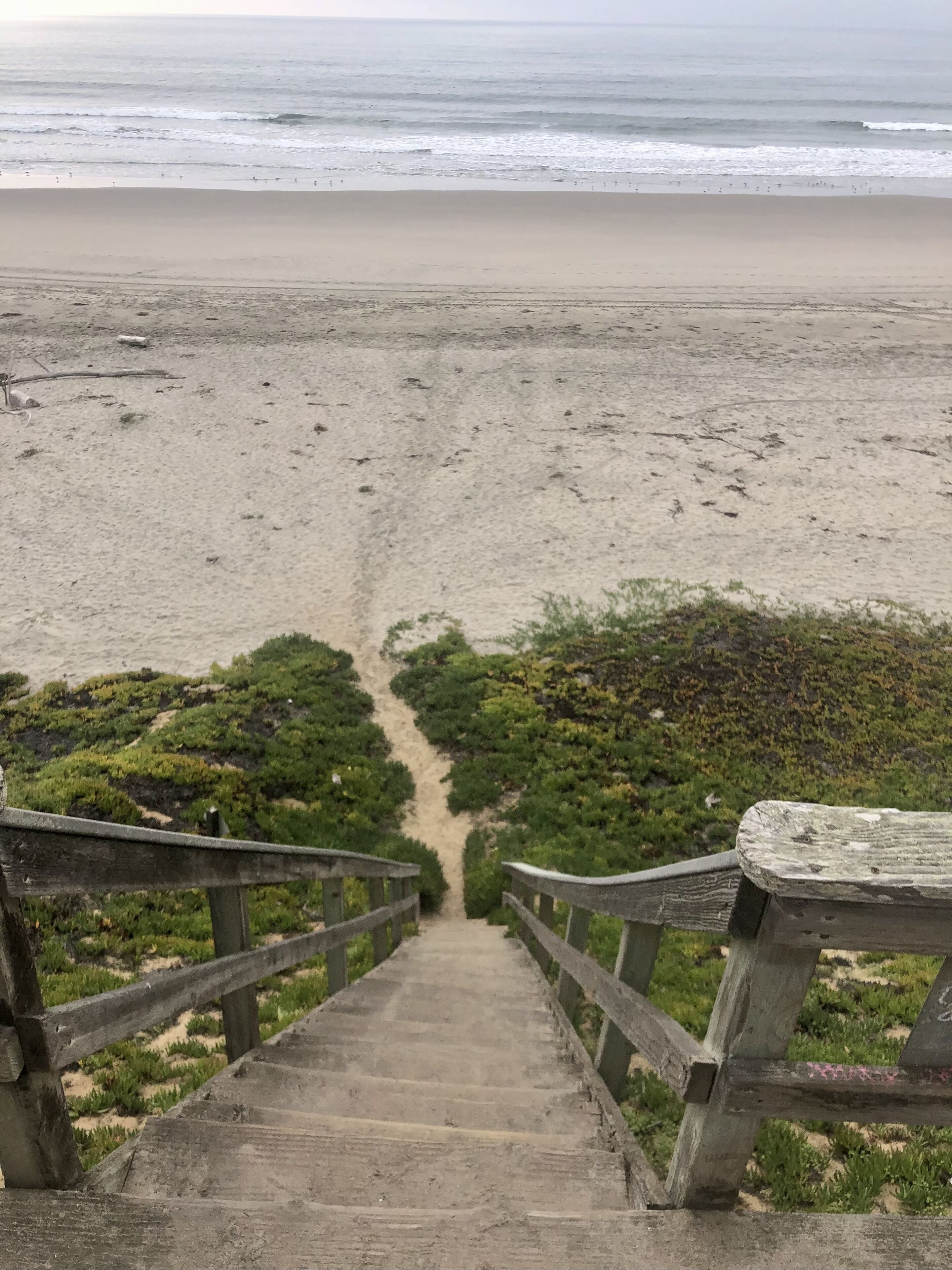 Un escalier en béton menant à une plage, avec une rambarde en bois d’un côté.