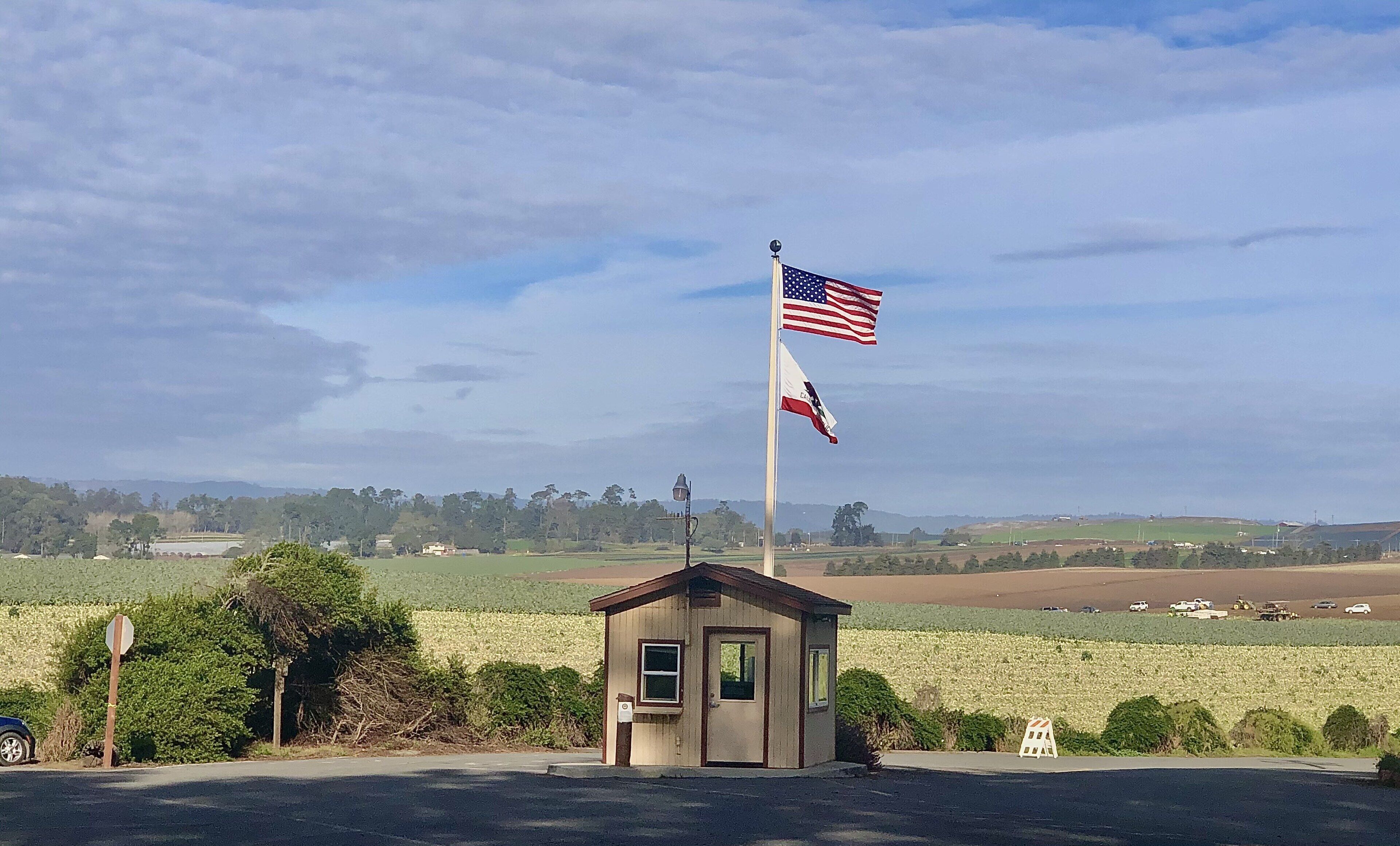 A small building with a flagpole, a flag, and a rural landscape in the background.
