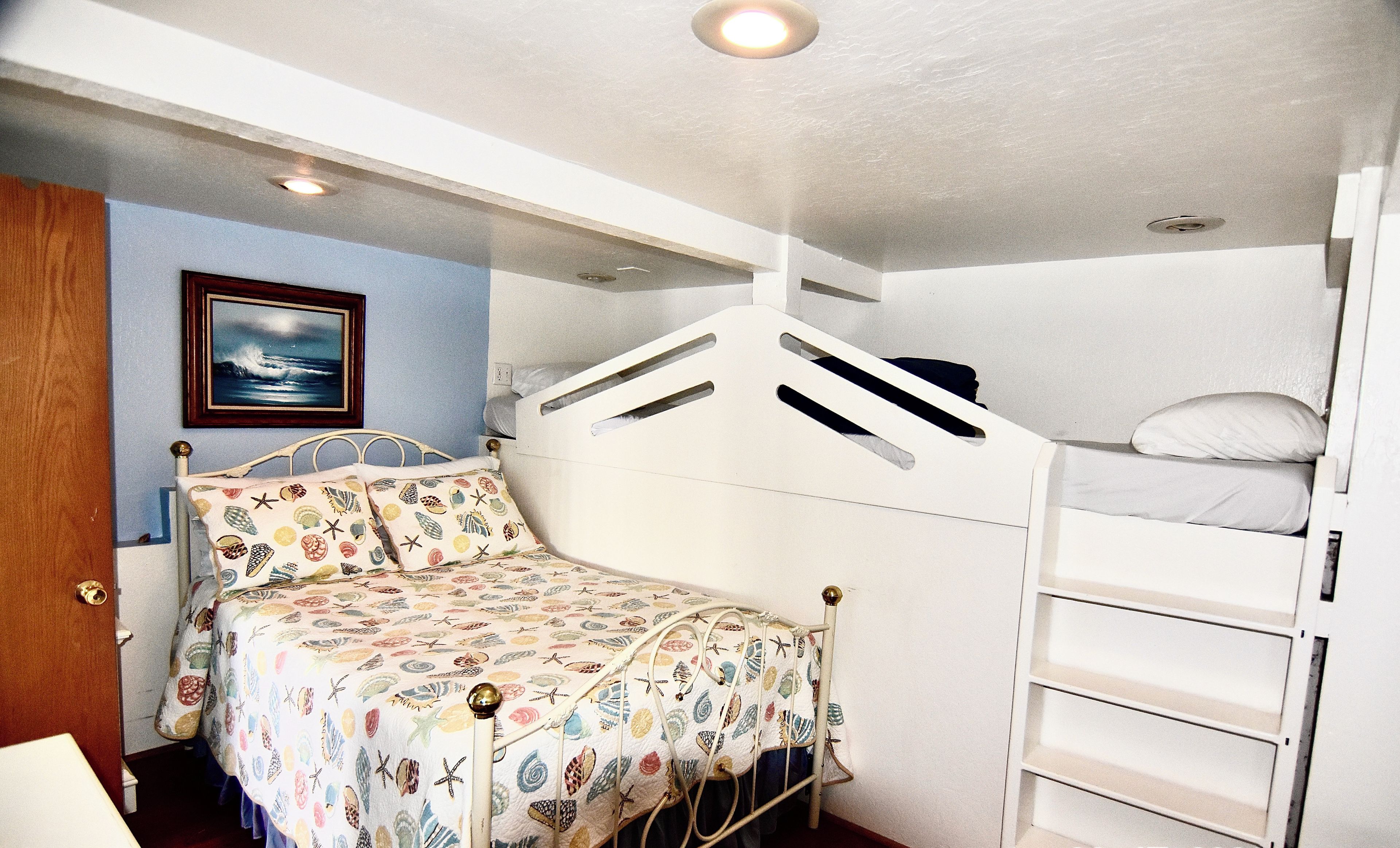 A bunk bed with a patterned bedspread, a small bedside table, and a framed picture on the wall.