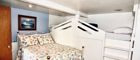 A bunk bed with a patterned bedspread, a small bedside table, and a framed picture on the wall.