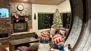 A cozy living room with a stone fireplace, a Christmas tree, and a large mirror reflecting the scene. - Stunning cabin in Torreon with unbeatable views—your search ends here! (Show Low)