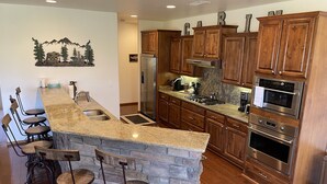 A kitchen with granite countertops, wooden cabinets, a built-in island with bar stools, stainless steel appliances, and a decorative wall piece. - Stunning cabin in Torreon with unbeatable views—your search ends here! (Show Low)