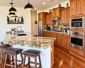 A kitchen with wooden cabinets, a granite countertop, stainless steel appliances, and a bar stool seating area. - Stunning cabin in Torreon with unbeatable views—your search ends here! (Show Low)