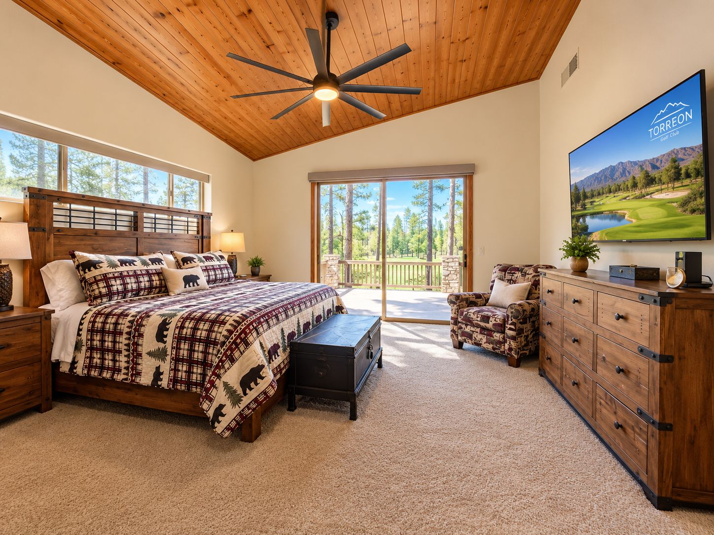 A bedroom with a large bed, a ceiling fan, a TV, and a view of the outdoors.