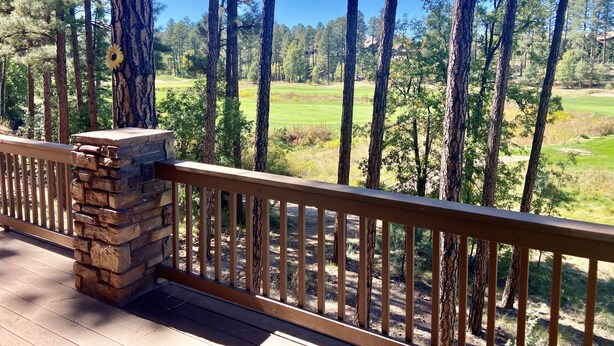 A wooden deck with a stone pillar, overlooking a golf course surrounded by tall pine trees. - Stunning cabin in Torreon with unbeatable views—your search ends here! (Show Low)