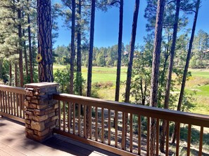 A wooden deck with a stone pillar, overlooking a golf course surrounded by tall pine trees. - Stunning cabin in Torreon with unbeatable views—your search ends here! (Show Low)