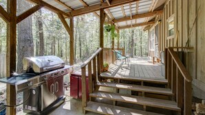 A covered outdoor deck with a grill, steps, and a chair.