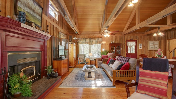 A cozy cabin interior with a fireplace, wooden furniture, and a large window providing natural light.