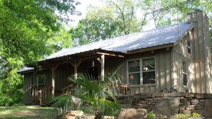 A rustic cabin with a porch, stone foundation, and a large window.