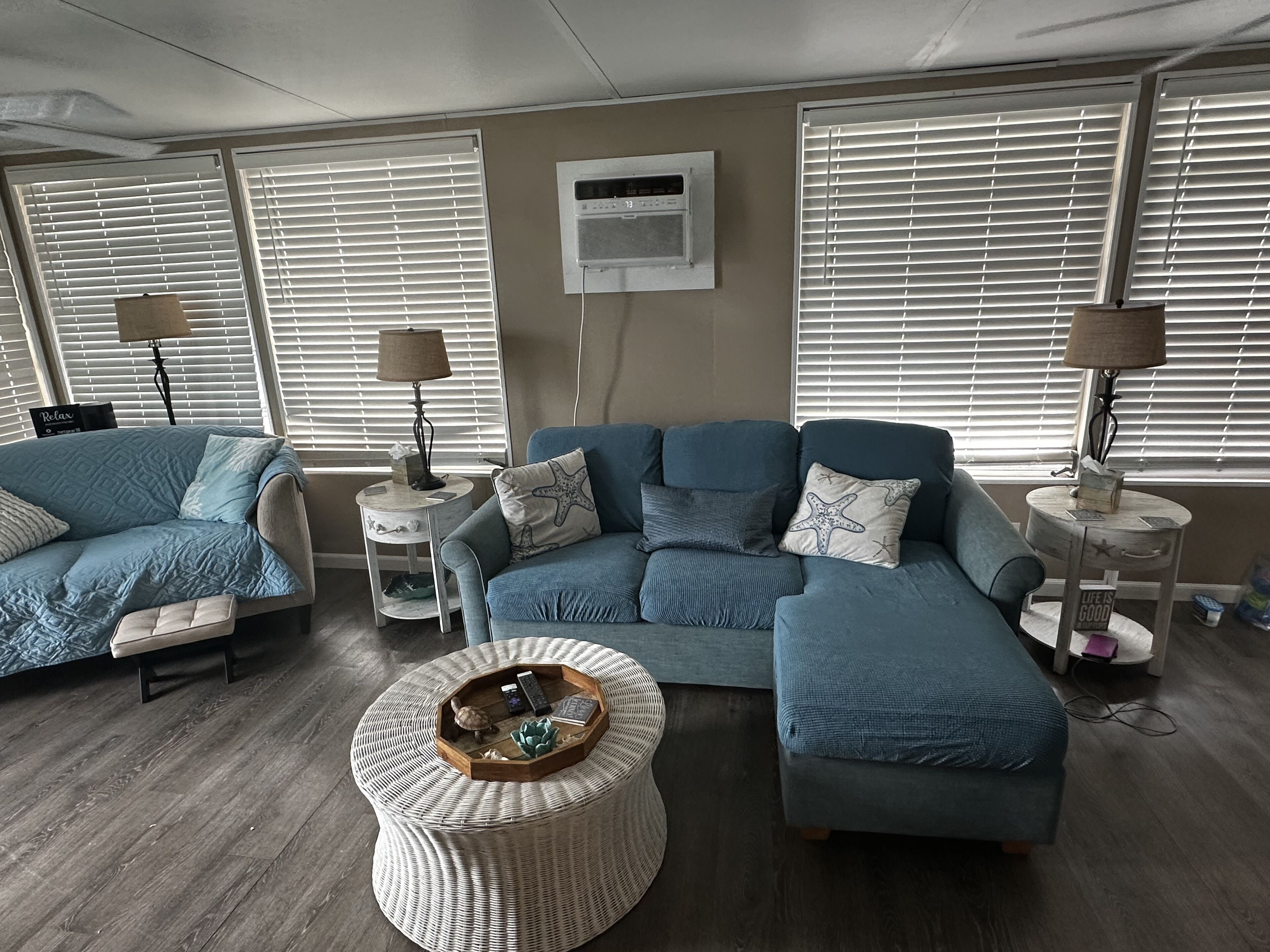 A living room with a sectional sofa, a round ottoman, and a wall-mounted air conditioner.