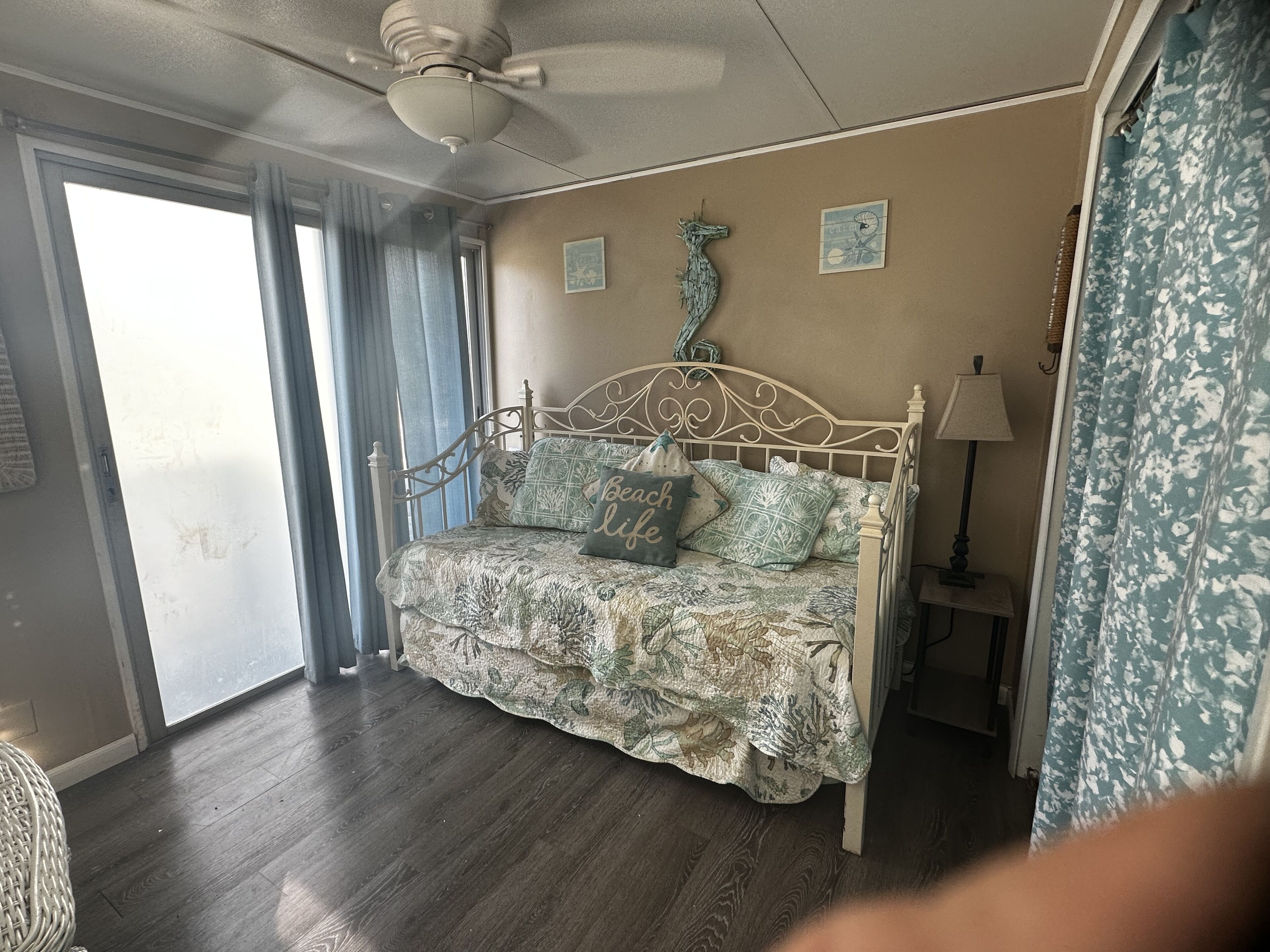 Une chambre à coucher avec un lit, un ventilateur de plafond, une lampe et une fenêtre avec des rideaux.