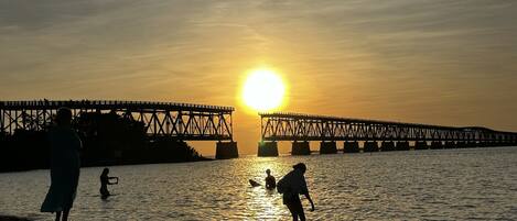 Un atardecer sobre una masa de agua con un puente al fondo.