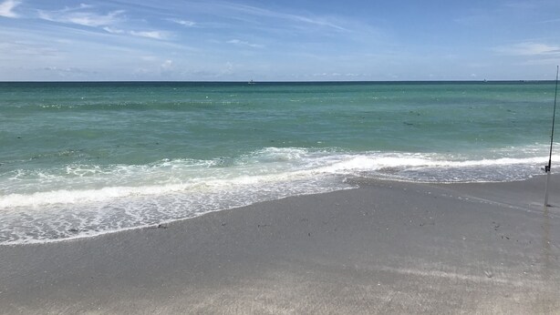 A beach with a fishing rod on the sand, clear blue sky, and calm sea.