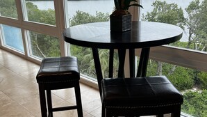 A room with a round table and two chairs, a potted plant on the table, and a view of a body of water through large windows.