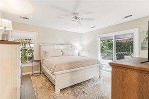 Relax in this serene bedroom with a large bed, ceiling fan, and a window offering a view of the outdoors.