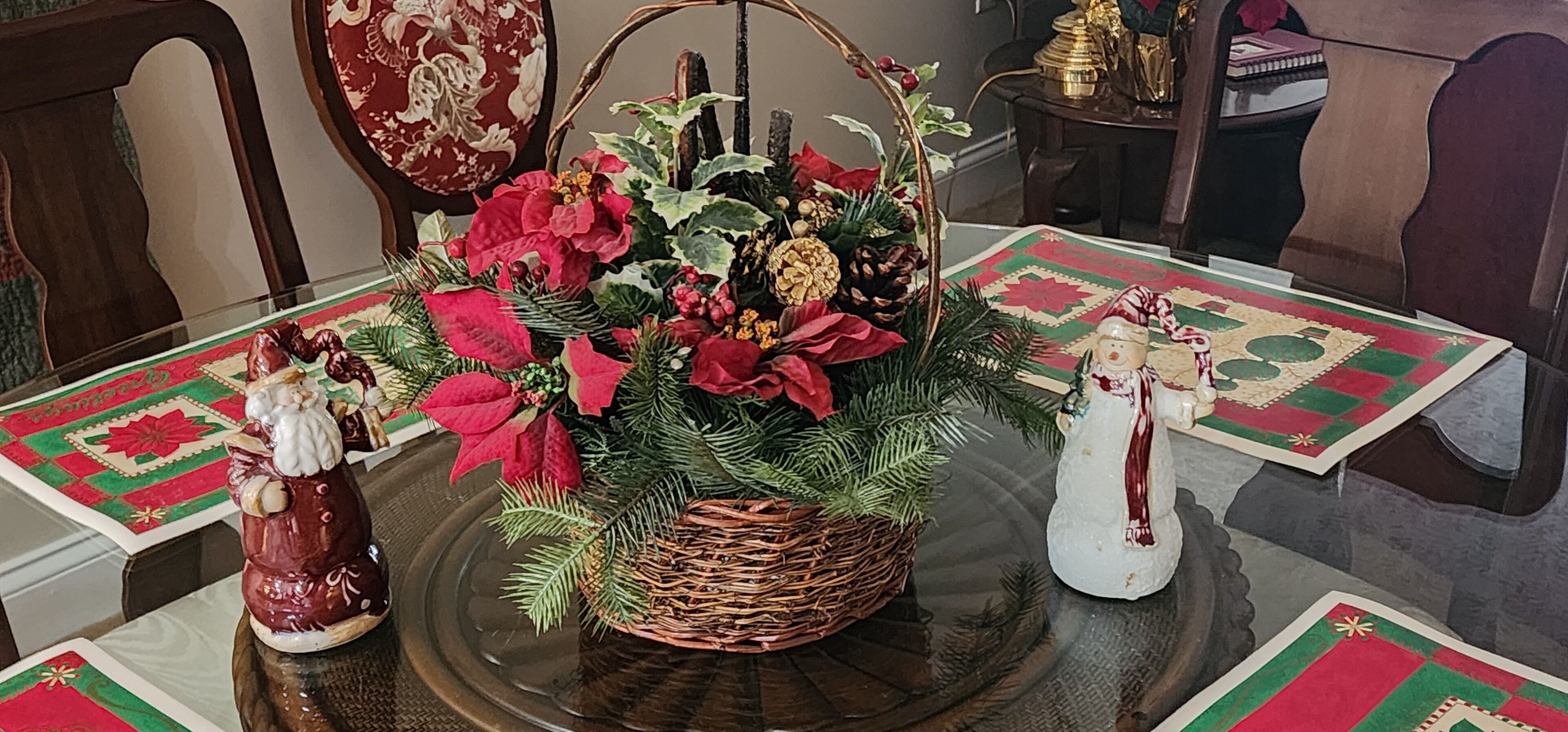 Una mesa de comedor con un centro de poinsettias y ramas de pino, rodeada de sillas y un plato decorativo.