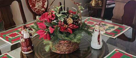 Una mesa de comedor con un centro de poinsettias y ramas de pino, rodeada de sillas y un plato decorativo.