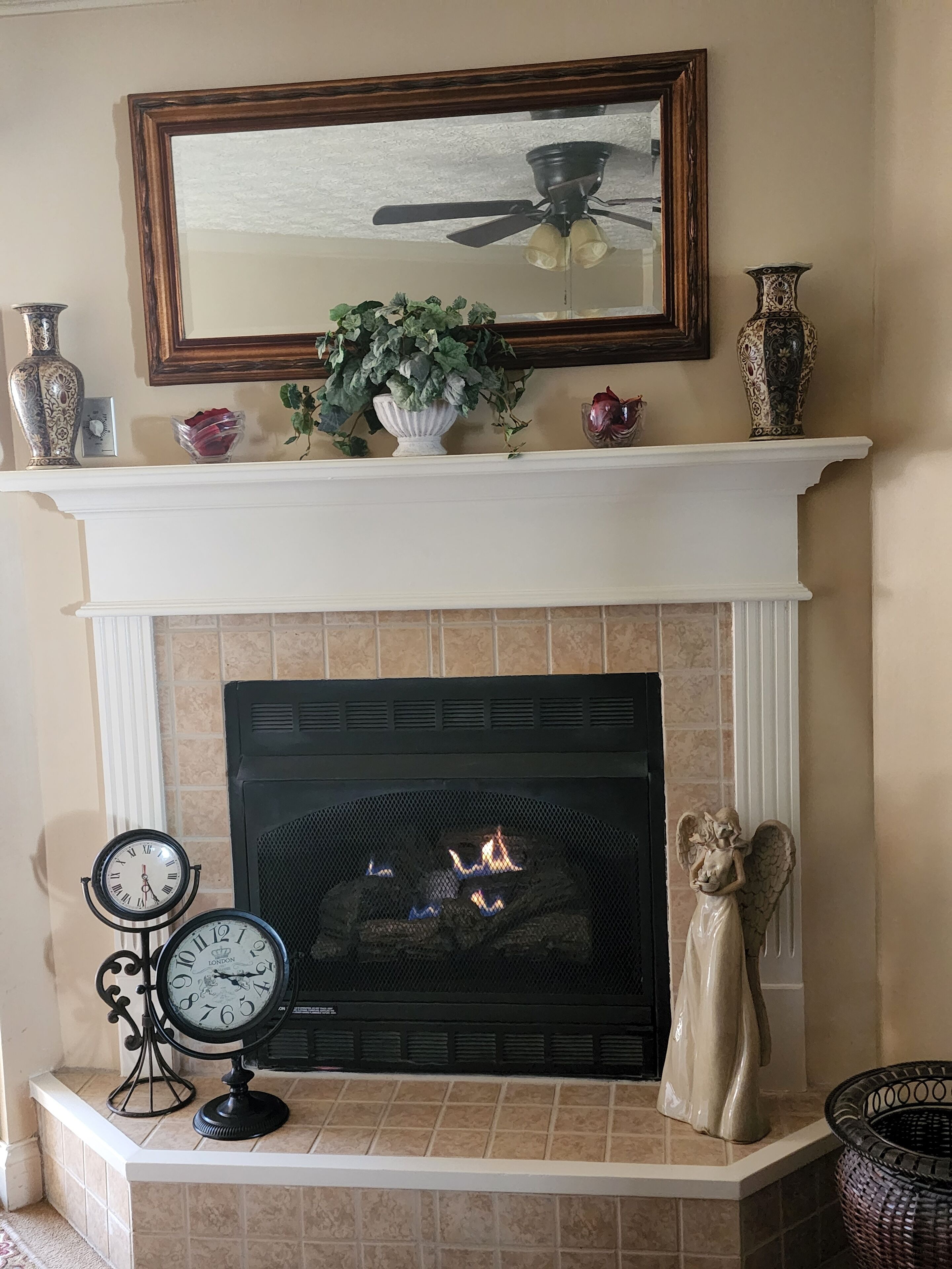 Una chimenea con repisa, un reloj y una estatua decorativa de un ángel.