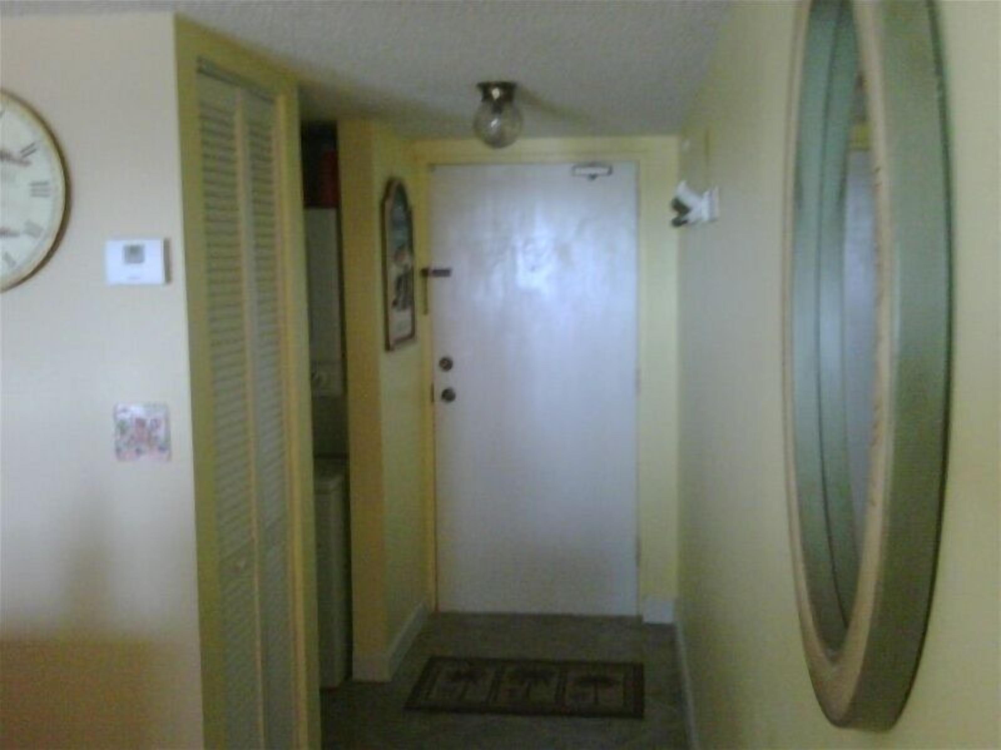 A hallway with a closed door, a clock on the wall, and a mirror on the right.