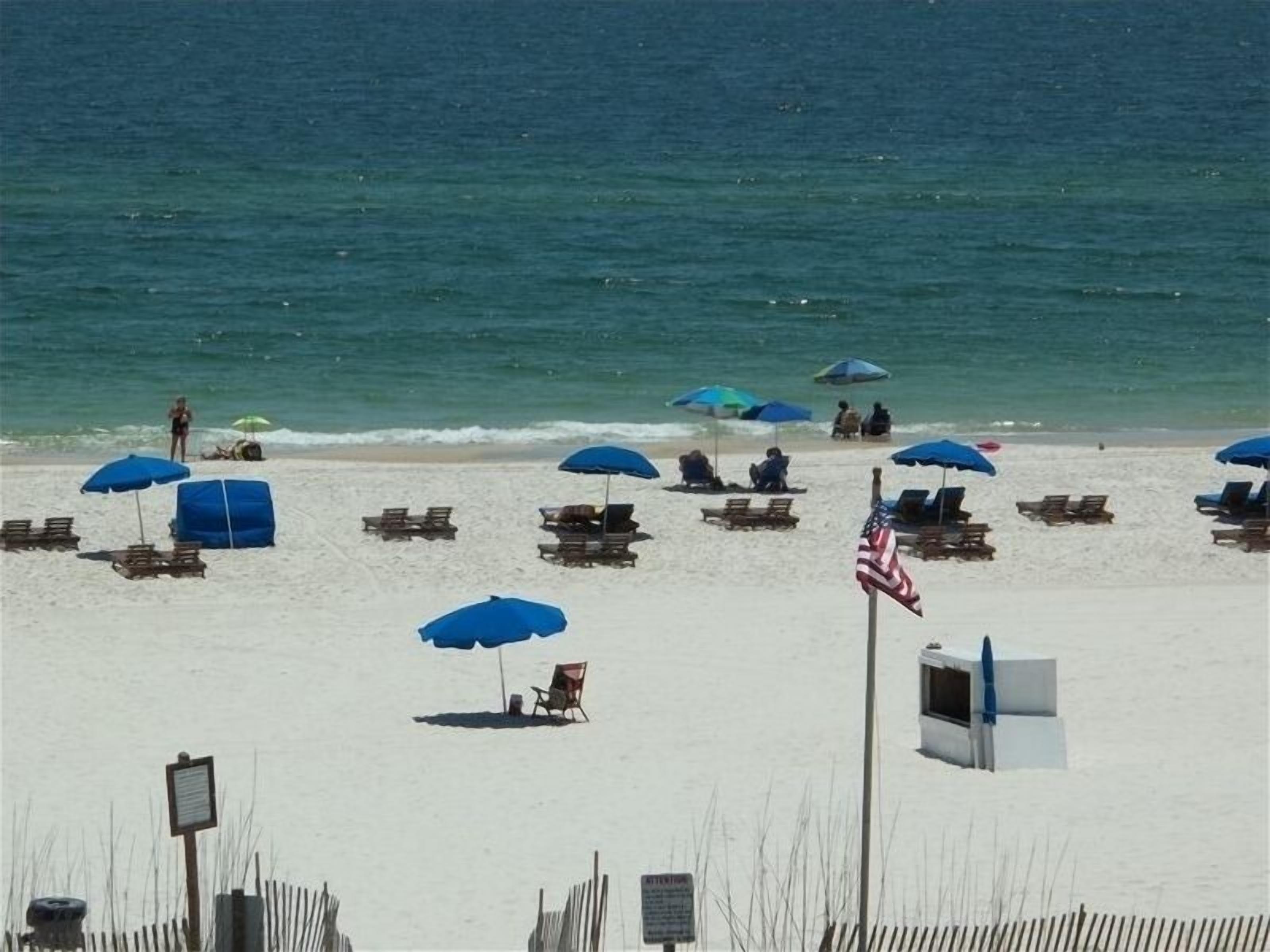 A beach with rows of sun loungers and umbrellas, a flag, and a fence.