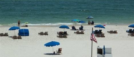 A beach with rows of sun loungers and umbrellas, a flag, and a fence.