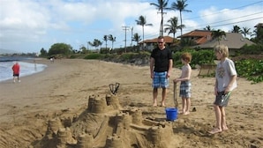 Una playa arenosa con un gran castillo de arena y un cubo azul.