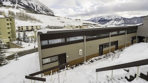 Ein Hotel mit modernem Design, das mehrere Etagen und ein flaches Dach aufweist. Das Gebäude wird von schneebedeckten Bergen und einem klaren Himmel umgeben.