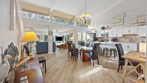 Eine geräumige Küche mit hohen Decken, ein Essbereich mit modernen Möbeln und ein Ausblick ins Freie durch große Fenster.