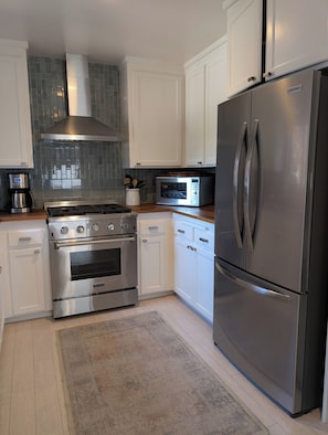 A modern kitchen with stainless steel appliances, white cabinetry, a tiled backsplash, and a built-in microwave.