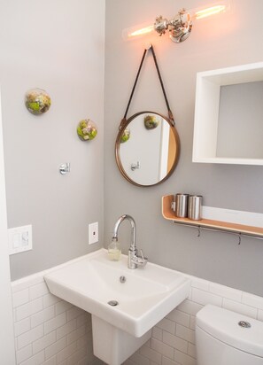 A bathroom with a white sink, a mirror, a toilet, and a shelf with toiletries.