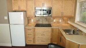 A compact kitchen with wooden cabinets, a stainless steel microwave, and a white refrigerator.