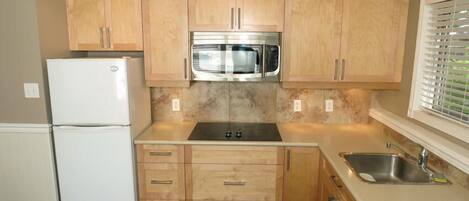 Cocina compacta con armarios de madera, microondas de acero inoxidable y refrigerador blanco.