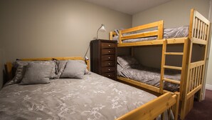 A bunk bed room with a wooden ladder, a desk with a lamp, and a dresser.
