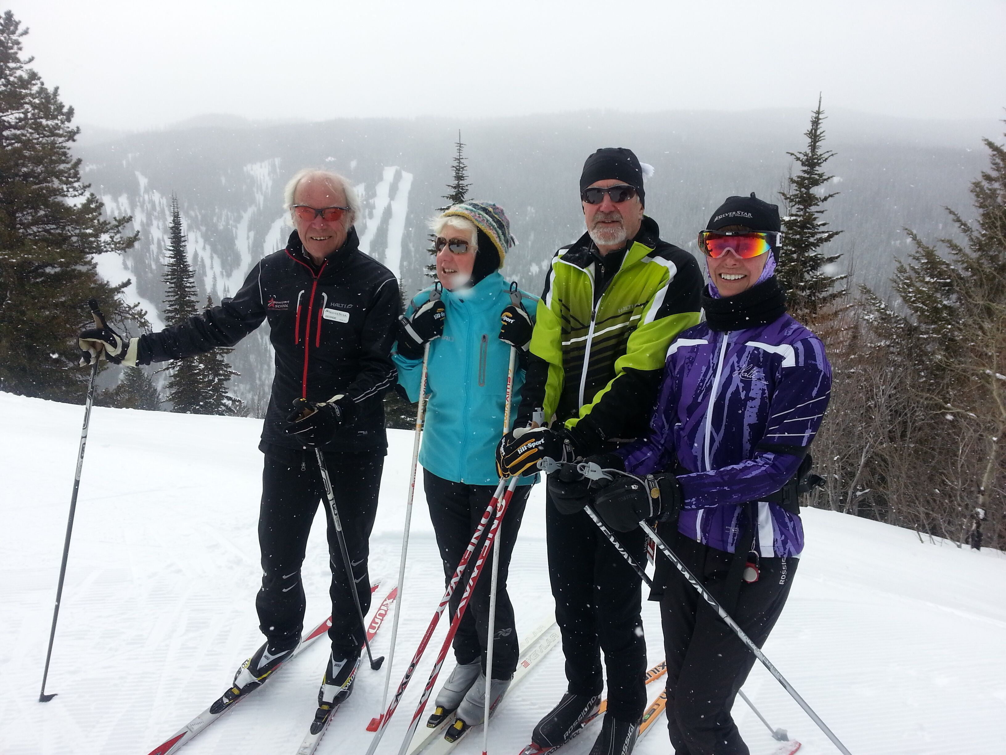 Quatre personnes font du ski sur une pente enneigée, avec des arbres en arrière-plan.